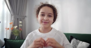Güzel, mutlu, şirin, sevimli bir çocuk. Sevimli bir çocuk. Parmaklarıyla kalp şekli oluştururken görülüyor. Sevgi, şefkat, aile bağı, bağış işareti, evlat edinme ve velayet.