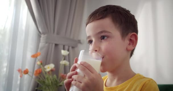 ミルクを飲んでいる少年のハンサム 朝食の子供を食べる 健康的な子供を食べる キッチンの小さな少年はヨーグルトミルクを飲み 唇をライセンスした 朝食を食べるケフィアを笑顔にするハッピーガール 4Kについて — ストック動画