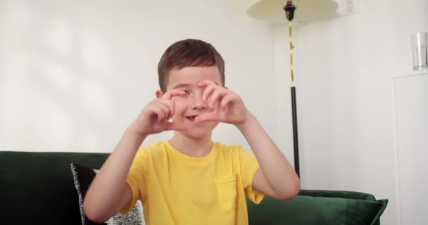 美しい幸せな小さなかわいい子供の顔は 心臓の形を作る接合された指を通して見た愛らしい男の子の顔を閉じます 家族の絆 寄付のサイン 養子縁組 親権のシンボル 4Kについて — ストック動画