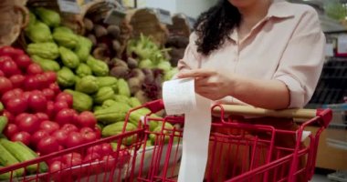 Sebze geçmişi olan bir kadın alışveriş merkezinde alışveriş yaptıktan sonra bakkal arabasındaki Sevgili Miktar faturasını kontrol ederek çekleri kontrol ediyor. Gıda fiyatlarında artış. Bakkal arabasını kontrol eden kadın.