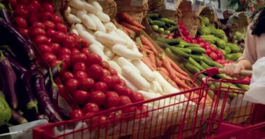 Güzel, genç, esmer, güzel bir kadın marketten yiyecek, domates alıyor. Kız ürünleri, sebzeleri, meyveleri dükkandan seçiyor. Alışveriş, vegan satış konsepti. 4K