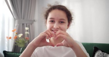 Güzel, mutlu, şirin bir çocuk. Sevimli bir kız çocuğu parmaklarıyla kalp şekli verirken görülüyor. Yaklaş. Aşkın sembolü, bağlılık, aile bağı, bağış işareti, evlat edinme ve velayet. 4K.