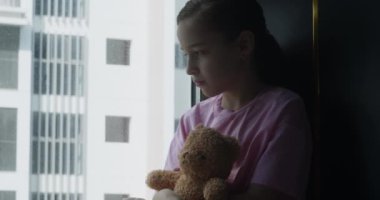 Üzgün çocuk. Karanlıktaki çocuk korkusu. Şirin küçük kız elinde bir oyuncakla odasında üzgün. Depresyondaki çocuk elinde oyuncak bir ayıyla odada. Aile içi şiddet kavramı. Portre çocuğu üzgün..