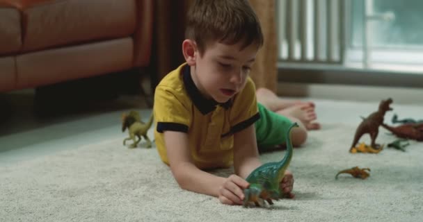 幸せな小さな子供たちは一緒に家で楽しんでいる古生物学を説明します 幼い大人の妹とかわいい就学前の子供の弟を愛する恐竜のおもちゃを話して暖かい床に座っています — ストック動画