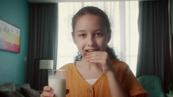 かわいい美しい子供は牛乳を飲んで 自宅でクラッカークッキーを食べています 朝食を食べる子供の健康的な食べ物は子供の頃の夢です キッチンにいる女の子は 牛乳と笑顔を飲む ポジティブな子供の笑顔 — ストック動画