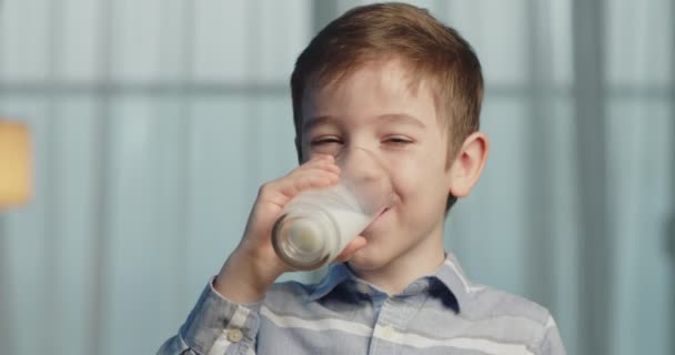 可爱的孩子喝牛奶健康的吃早餐的孩子梦想的概念 儿子小男孩在厨房里喝酸奶牛奶 舔她的嘴唇 — 图库视频影像