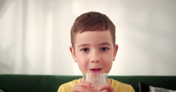 かわいいハンサムな子供は牛乳を飲んでいます 朝食を食べる子供を健康的に食べる子供の夢のコンセプト キッチンで面白い男の子はヨーグルトミルクを飲み 彼女の唇をライセンスします 朝食を持って微笑んでいる敏感な子供 4Kについて — ストック動画