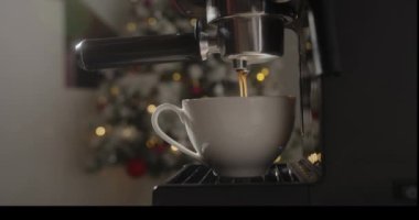 Makineden fincana dökülen bir rulo kahve. Ev yapımı sıcak kapuçino bir Noel ağacı ve Noel ışıklarına karşı. Taze öğütülmüş kahve akar. Sabahları içerim.