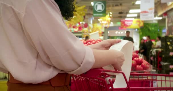 レッドトマトのバックグラウンドでショッピングの後 女性の背面のビューは 食料品カートで親愛なる金額の請求書をチェックすることによって モールでの食料品の買い物の後ろのチェック 食糧価格の上昇 お金を費やすこと — ストック動画