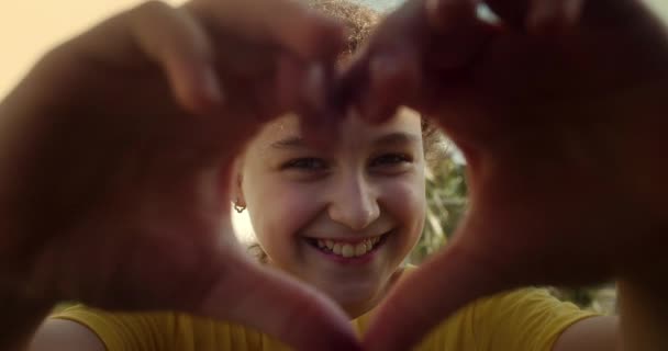 小女孩让签署爱的手日落 小孩在天空中手牵手 签署心的象征爱 在太阳近照下的心脏轮廓手牵手 手塑造心脏 手指间的阳光 — 图库视频影像