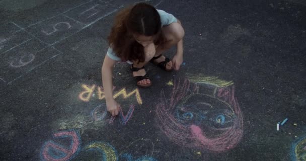 俯瞰可爱而悲伤的小女孩用粉笔在柏油路上画出和平 关于悲伤的孩子用粉笔和平书写的头像 抗议战争 俄国入侵乌克兰 — 图库视频影像