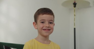 Evdeki küçük okul çocuğunun portresi. Öğrenci, çocuk, yetim, çocuk, çocuk, yetim çocuk. Kanepede oturmuş kameraya gülümsüyor. 4K.