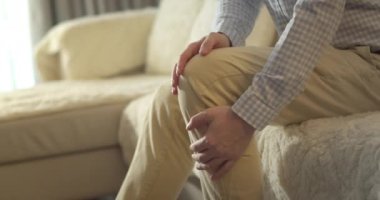 Kapatın. Erkek eller, evdeki oturma odasında kanepede otururken diz kaslarına masaj yapıyor. Yaşlı siyahi adam diz eklem ağrısı çekiyor, yürüyemiyor, hastalık, kramp, romatizma.