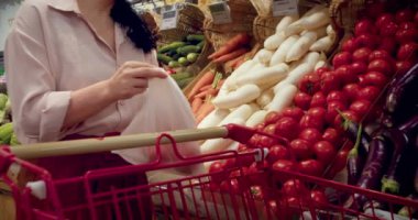 Alışveriş, vejetaryen satış konsepti. Kız marketten sebze, sebze ve meyve seçiyor. 4K 'de ağır çekim. Kadın marketten yiyecek, domates alıyor, markette domatesleri sepete koyuyor