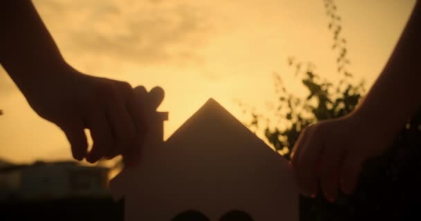 Χέρια Της Οικογένειας Κρατάνε Ένα Χάρτινο Σπίτι Ηλιοβασίλεμα Ήλιος Λάμπει — Αρχείο Βίντεο