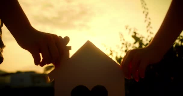 家族の手は日没に紙の家を持ち 太陽は窓から輝いています 家のシンボル 家族のために家を建てるという考え方 家を買う夢を見る 4Kについて — ストック動画