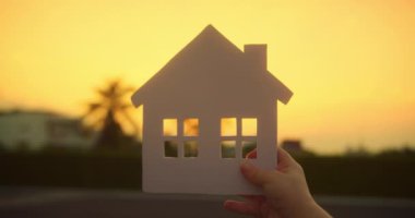 Kağıt ev aile fertleri, güneş yakın planda parlıyor. Gün batımında kağıt evde. Sembol ev, aile rahatlığı, mutluluk. Konsept bina ailesi, çocuğum. Rüya evi satın al. Emlak sigortası.