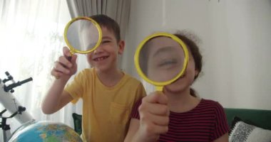 Çocuk aktiviteleri. Neşeli ve tatlı bir gülümseme, elinde büyüteç, oyun, kahkaha ve kameraya bakan, gün batımının altında ev ortamında oturan neşeli bir kız ve oğlan
