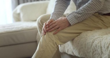 Kapatın. Erkek eller, evdeki oturma odasında kanepede otururken diz kaslarına masaj yapıyor. Yaşlı siyahi adam diz eklem ağrısı çekiyor, yürüyemiyor, hastalık, kramp, romatizma.