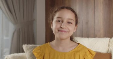 Portre Komik küçük kız kameraya bakıyor evde kanepede oturuyor, güzel yüzlü şirin çocuk kanepede oturuyor. Mutlu bir çocukluk kavramı.