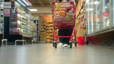 Yavaş çekimde bir süpermarkette alışveriş arabasını iten kadına yaklaş. Market alışverişi kavramı