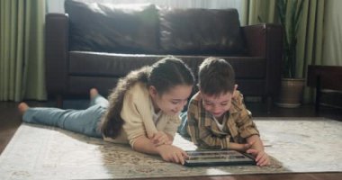 Farklı yaşlardaki sevimli çocuklar dijital cihazlarla, interneti mobil dijital cihazlarla, kız ve erkek çocuk halının üzerinde cep telefonuyla oynuyorlar. 4K.