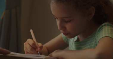 Evde bir masada oturmuş ders çalışan tatlı bir ilkokul öğrencisi, ödev yapan bir çocuk, evde tek başına okuyan bir okul çocuğu, ilkokul çocuğu, ilkokul konsepti. 4K