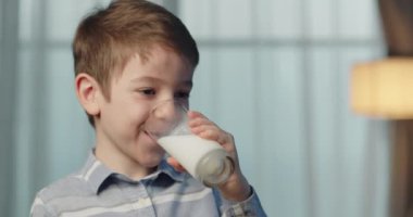 Tatlı çocuk süt içiyor. Sağlıklı beslenen bir çocuk kahvaltılık çocuk rüyası kavramı. Mutfaktaki küçük çocuk yoğurt sütü içip dudaklarını yalıyor. Kahvaltını yaparken gülümseyen pozitif çocuk. 4K.