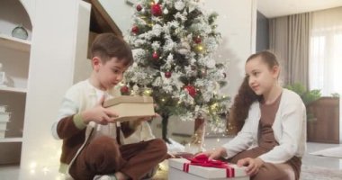 Noel hediyesi kutusunu açan yakışıklı ve şaşkın çocuk şöminenin yanındaki geleneksel oturma odasında oturuyor. Portre küçük çocuk, mutlu sürpriz çocuk