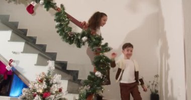 Mutlu çocuklar Noel hediyesi kutularını, çocukları ve Noel hediyelerini Noel ağacının yanındaki dekore edilmiş geleneksel oturma odasında açmak için merdivenlerden aşağı koşuyorlar. Mutlu çocuklar sürprizle mutlu olurlar.