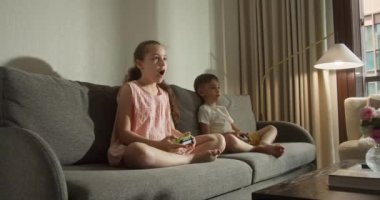 Çocuklar multimedya oyunlarını sever. Sevimli küçük kız ve oğlan gülümsüyor, çocuklar TV 'de video oyunu oynuyor, oturma odasındaki kanepede oturmuş bilgisayar oyunları oynuyor. Bilgisayar oyunu oynayan çocuklar.