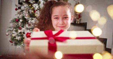 Noel Baba 'nın Noel Baba' sına gülümseyen mutlu portre evde Noel ağacının yanında otururken üzerinde güzel kırmızı bir fiyonk olan bir kutuda Noel hediyesi veriyor. Kış tatili