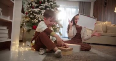 Noel hediyesi kutusunu açan yakışıklı ve şaşkın çocuk şöminenin yanındaki geleneksel oturma odasında oturuyor. Portre küçük çocuk, mutlu sürpriz çocuk