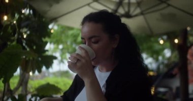 Güzel genç Hintli kadın rahatça oturuyor ve dışarıdaki bir kafede kahve içiyor. Çekici, genç bir bayan sıcak kahve ya da çay içerek dışarıya bakıyor.