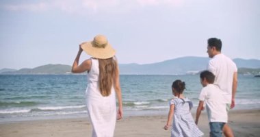 Asyalı genç mutlu aile akşamları sahilde tatilin tadını çıkarıyor. Baba, anne ve çocuklar gün batımında deniz kenarında yürürken rahatlar. Hayat tarzı seyahat tatil yaz tatili konsepti. 4k ağır çekim