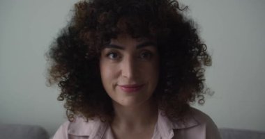 Yüz, esmer kıvırcık saçlı kadın. Güzel, kıvırcık saçlı, kameraya bakıp mutlu gülümseyen, mutlu, sağlıklı gülümseyen neşeli bir kadının portresini yakından çek. 4K.
