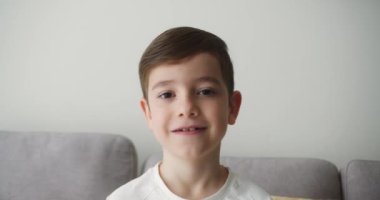 Portre Komik küçük kız kameraya bakıyor evde kanepede oturuyor, güzel yüzlü şirin çocuk kanepede oturuyor. Mutlu bir çocukluk kavramı.