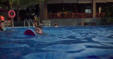 Yüzme gözlüklü çocuk yüzücü açık havuzda yüzüyor. Çocuk portresi, havuzda yüzen sevimli bir çocuk, açık havuzda kameraya bakan gülümseyen bir çocuk..