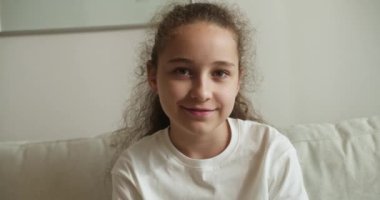 Portre Komik küçük kız kameraya bakıyor evde kanepede oturuyor, güzel yüzlü şirin çocuk kanepede oturuyor. Mutlu bir çocukluk kavramı.