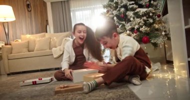 Noel hediyesi kutusunu açan mutlu çocuklar Noel ağacının yanındaki geleneksel oturma odasında oturuyorlar. Mutlu, sürpriz çocuklar sürpriz Noel 'le kutuları açıyor.