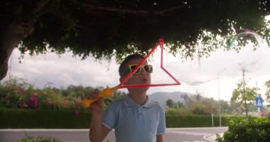 Joy Kid yaz günü sabun köpüğüyle oynuyor. Yeşil ağaçların arka planına sabun köpüğü üfleyen mutlu çocuk. Küçük çocuk doğada dinleniyor. Aile hafta sonu kavramı. Tatil sabun köpükleri
