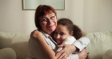 Sevgi dolu yaşlı büyükannenin yanaklarından öptüğü küçük 10 'lu yaşlarda bir torun, aile kanepeye oturur şefkat dolu bir anın tadını çıkarır, sevgi ve şefkat gösterir, bağlılık ve samimi duygular ifade eder.