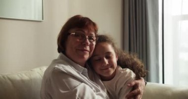 Sevgi dolu yaşlı büyükannenin yanaklarından öptüğü küçük 10 'lu yaşlarda bir torun, aile kanepeye oturur şefkat dolu bir anın tadını çıkarır, sevgi ve şefkat gösterir, bağlılık ve samimi duygular ifade eder.