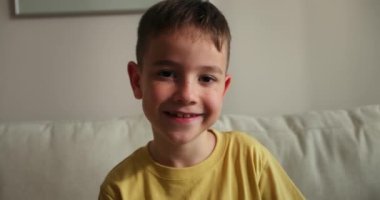 Çok mutlu bir çocuğun portresi, gülümseyen bir çocuk kameraya bakıyor, kanepede oturuyor, güzel bir yüzü olan tatlı bir çocuk kanepede oturuyor. Mutlu çocukluk kavramı. 4K.