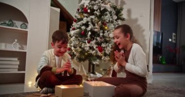 Noel hediyesi kutusunu açan mutlu çocuklar Noel ağacının yanındaki geleneksel oturma odasında oturuyorlar. Mutlu, sürpriz çocuklar sürpriz Noel 'le kutuları açıyor.