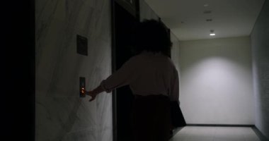 Bir iş kadını asansör düğmesine basar ve asansörü bekler. Tabletli gözlük takan kıvırcık saçlı bir kadın asansöre biner.
