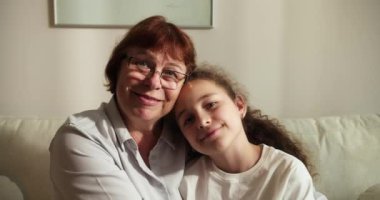 Sevgi dolu yaşlı büyükannenin yanaklarından öptüğü küçük 10 'lu yaşlarda bir torun, aile kanepeye oturur şefkat dolu bir anın tadını çıkarır, sevgi ve şefkat gösterir, bağlılık ve samimi duygular ifade eder.