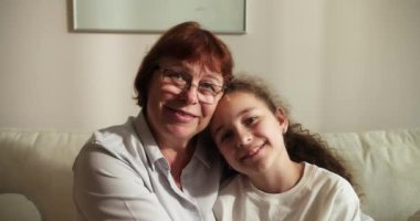 Sevgi dolu yaşlı büyükannenin yanaklarından öptüğü küçük 10 'lu yaşlarda bir torun, aile kanepeye oturur şefkat dolu bir anın tadını çıkarır, sevgi ve şefkat gösterir, bağlılık ve samimi duygular ifade eder.
