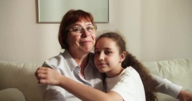 Sevgi dolu yaşlı büyükannenin yanaklarından öptüğü küçük 10 'lu yaşlarda bir torun, aile kanepeye oturur şefkat dolu bir anın tadını çıkarır, sevgi ve şefkat gösterir, bağlılık ve samimi duygular ifade eder.