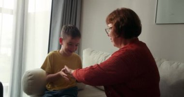 60 'lı yaşlarda neşeli bir büyükanne, küçük bir torun taşıyor, kız kollarını açıyor, uçak gibi uçtuğunu hayal ediyor, gülüyor, kameraya bakıyor, evdeki kanepede oturmuş eğleniyor. Aile tatili ve seyahat.